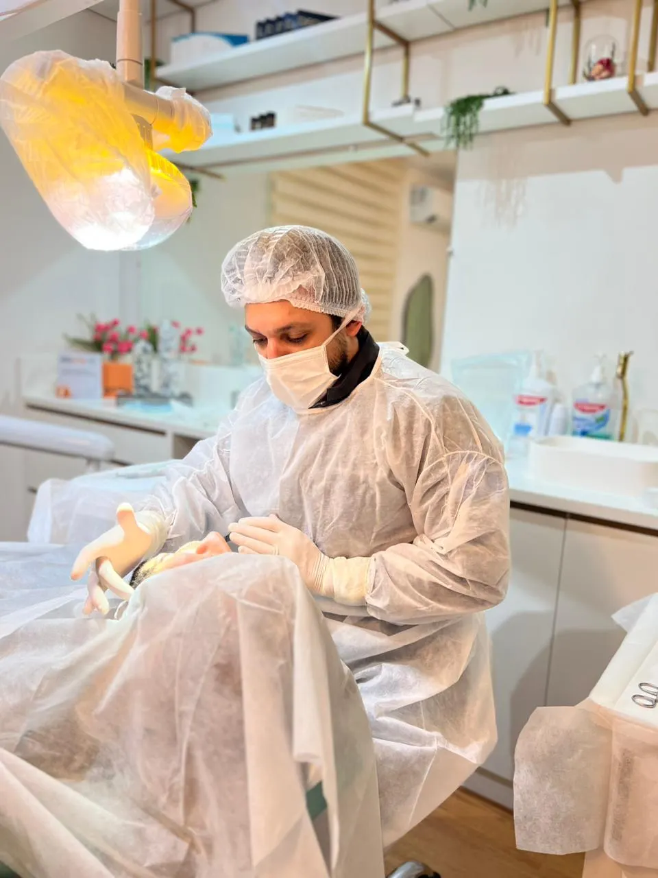 Cirurgião paramentado atendendo um paciente coberto por campo cirúrgico, na sala de procedimentos da clínica